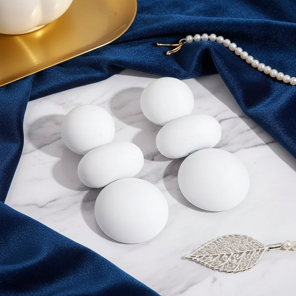 House of eLLe I'm Flexible white matte round earrings arranged on a marble surface with blue velvet and pearls.