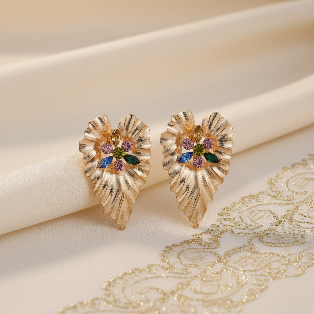 House of eLLe gold-toned leaf-shaped cluster earrings featuring colorful crystal accents on a draped fabric background