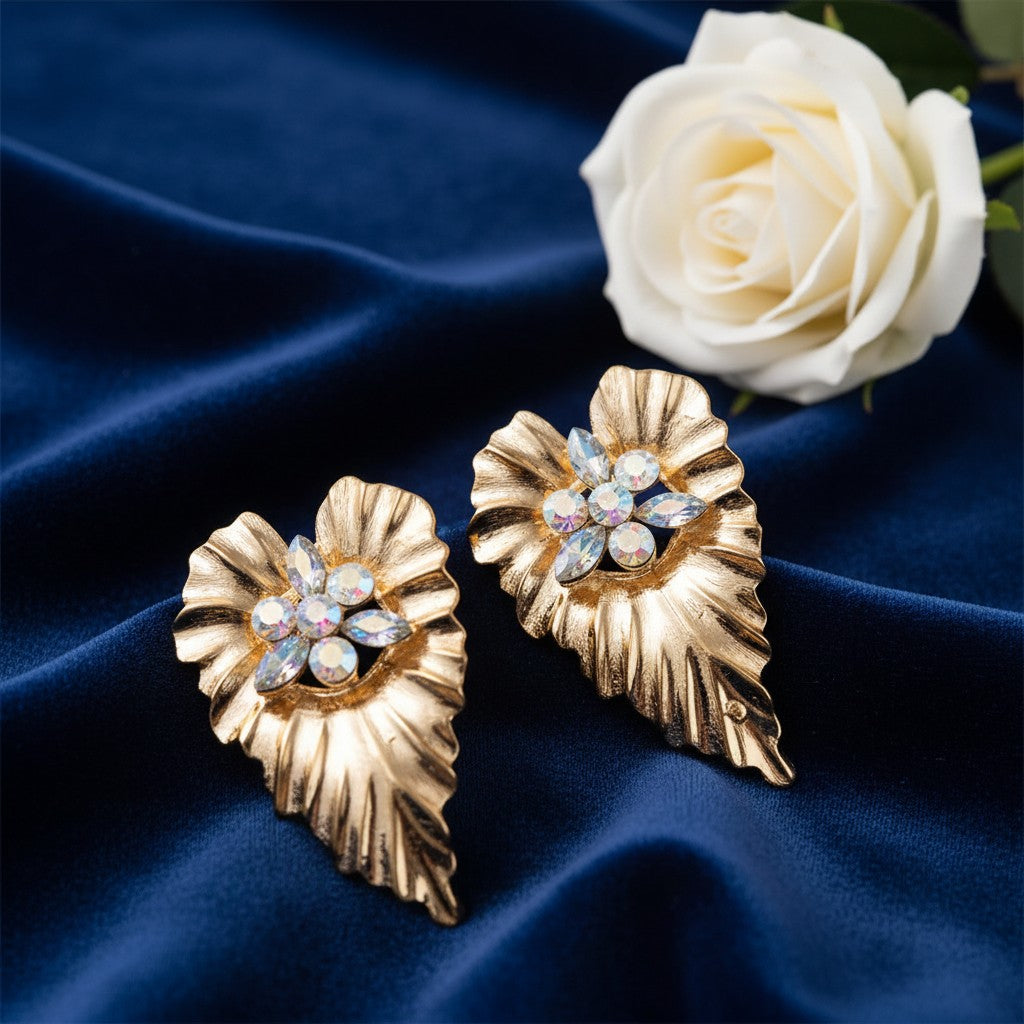 House of eLLe gold-tone leaf-shaped cluster earrings with iridescent white crystals on a navy blue velvet background.