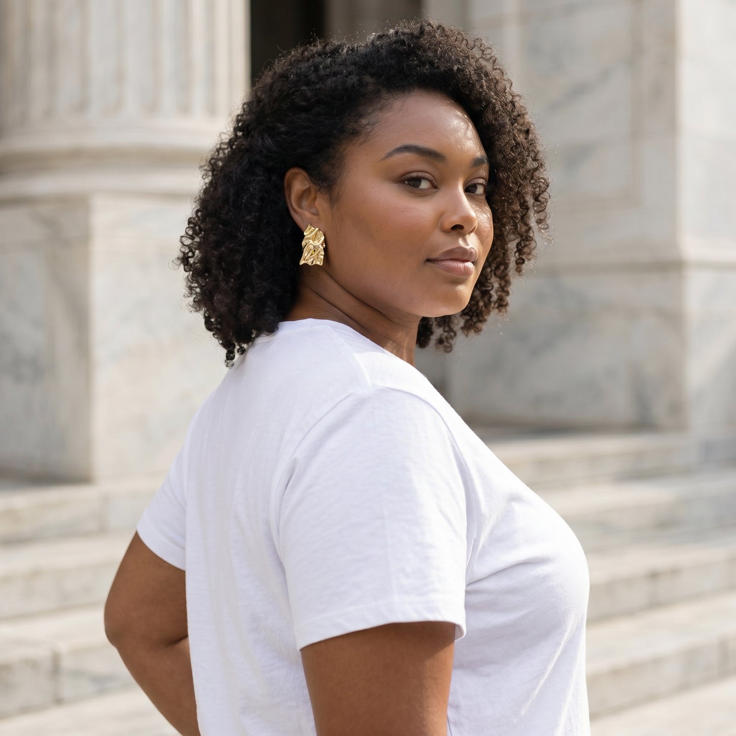 House of eLLe Living Life earrings in gold, abstract wavy design, statement earrings worn by a woman with curly hair.