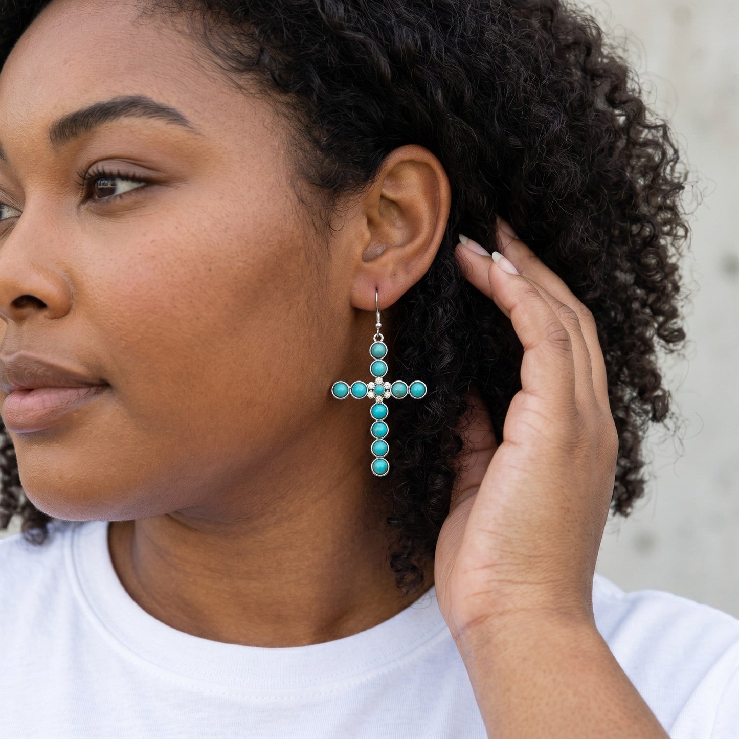 Model wearing House of eLLe turquoise cross earrings with silver accents on a drop hook style