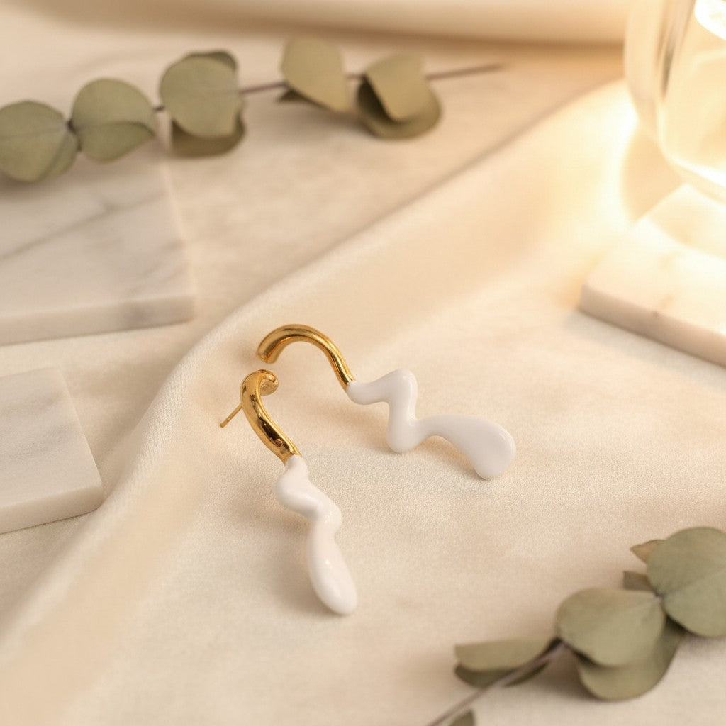 House of eLLe Dripped In Glam stainless-steel earrings featuring a gold curved top and white abstract drip design.