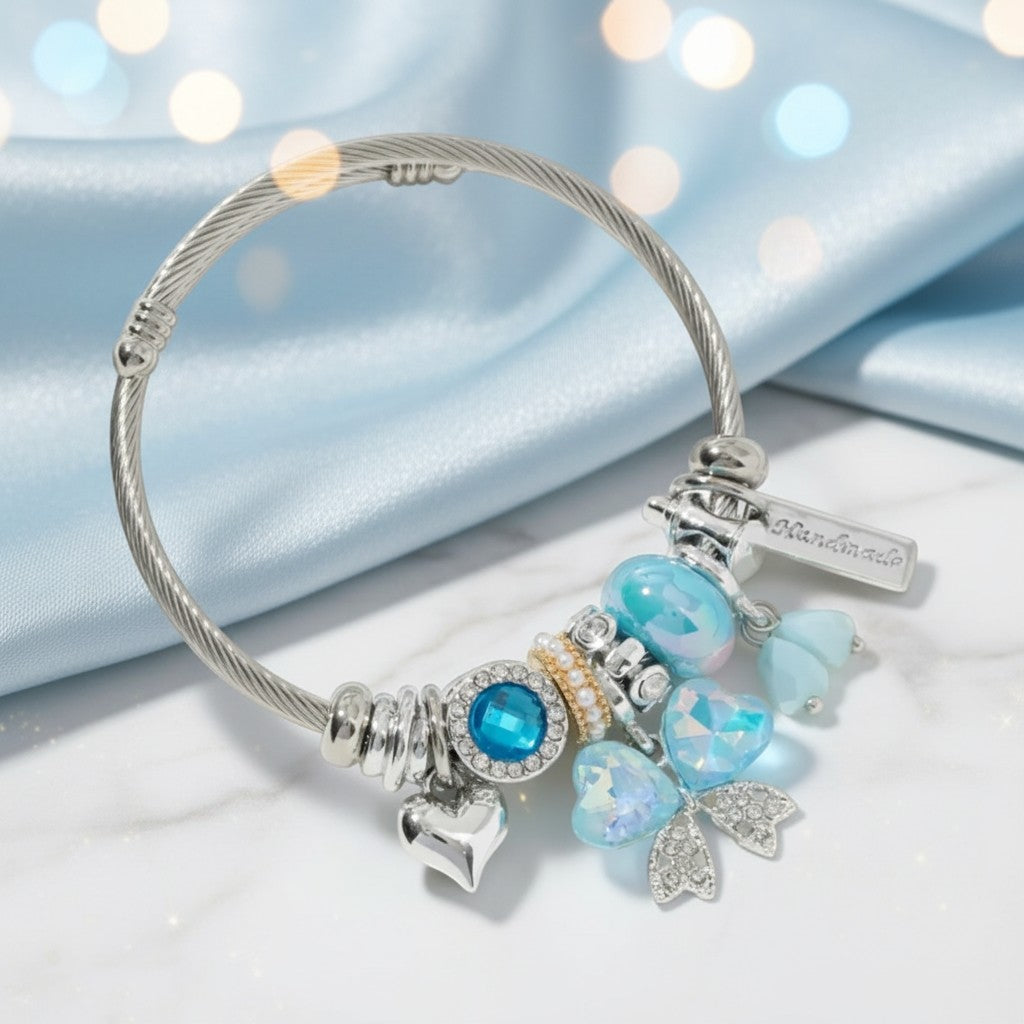 House of eLLe stainless steel charm bracelet featuring blue crystals, heart charms, and a bow design on silk fabric.