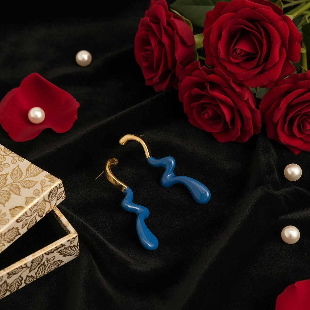 House of eLLe Dripped In Glam blue stainless-steel earrings with a wavy design on a black velvet background with roses.