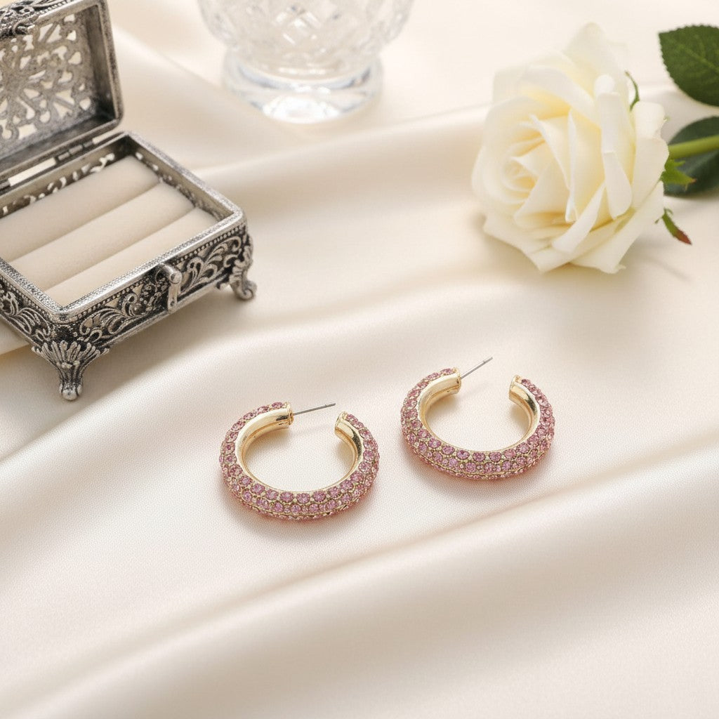 House of eLLe Party Time hoop earrings featuring blush pink rhinestones on a gold setting, displayed on satin fabric.