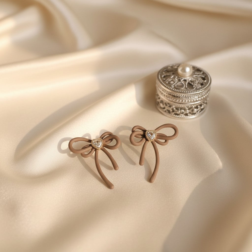 House of eLLe Cappuccino Bows earrings featuring matte brown ribbon shapes with a central heart-shaped crystal detail.
