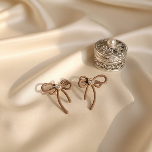 House of eLLe Cappuccino Bows earrings featuring matte brown ribbon shapes with a central heart-shaped crystal detail.