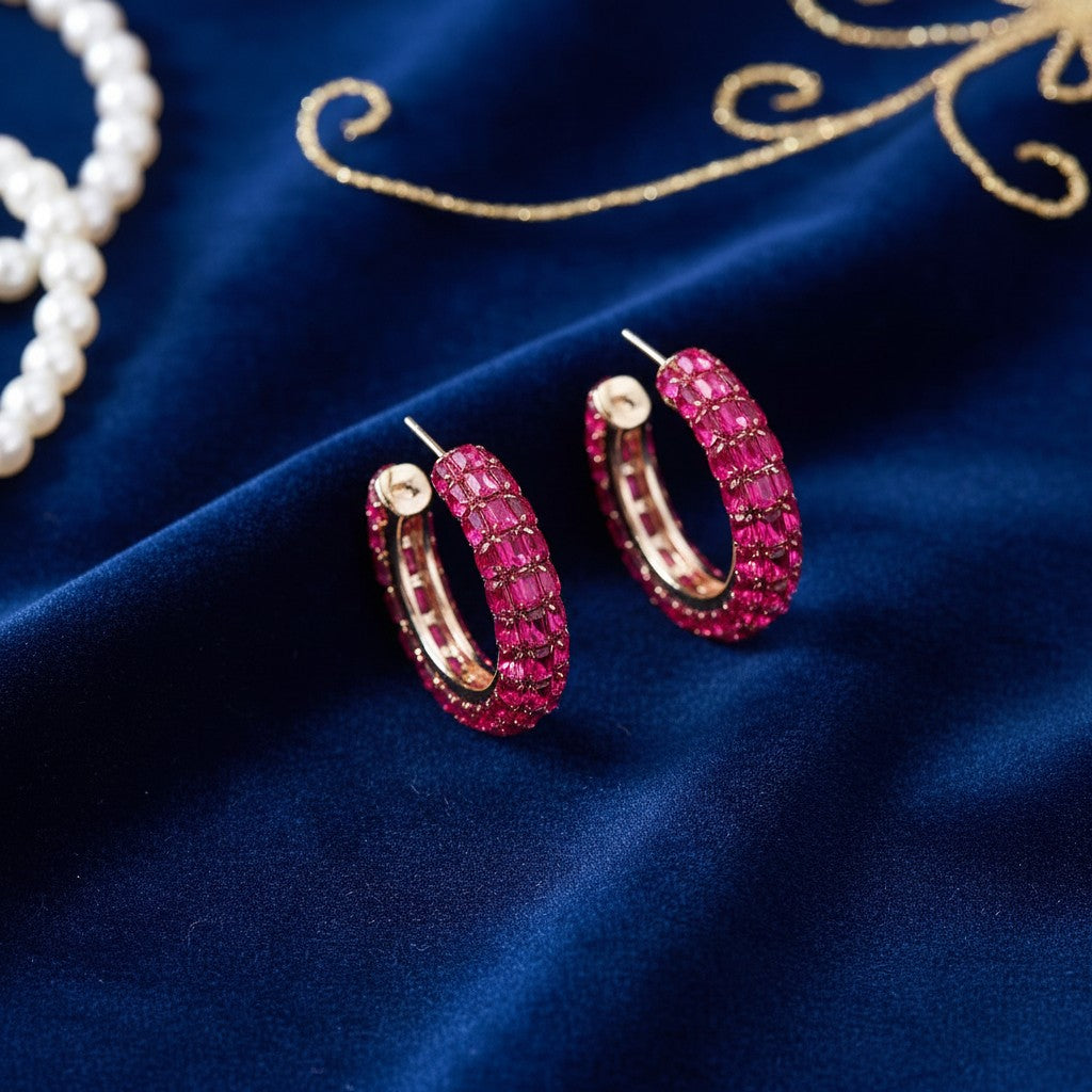 House of eLLe Life Of The Party hoop earrings featuring dark pink baguette crystals on a blue velvet background.