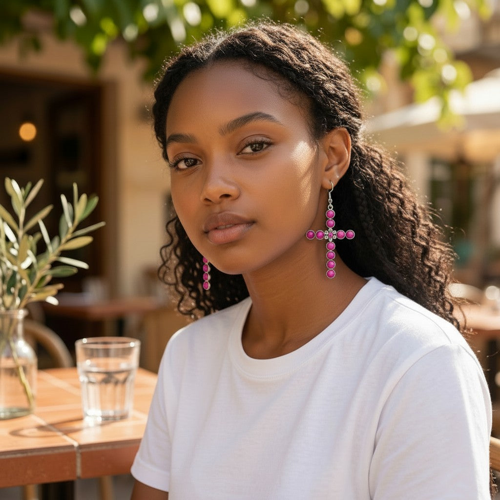 House of eLLe dark pink bling cross earrings worn by a woman in a white t-shirt at an outdoor cafe