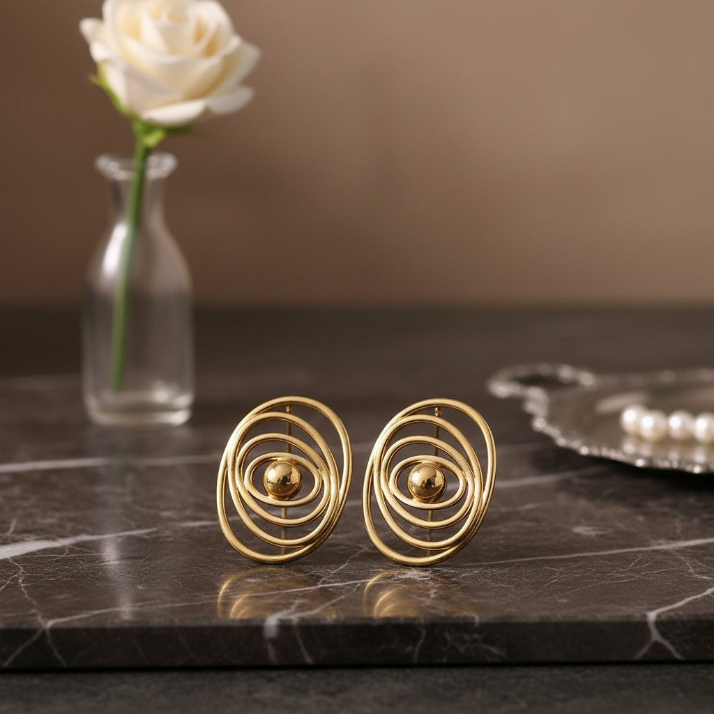 House of eLLe gold earrings featuring a modern concentric oval design with a central polished sphere on marble