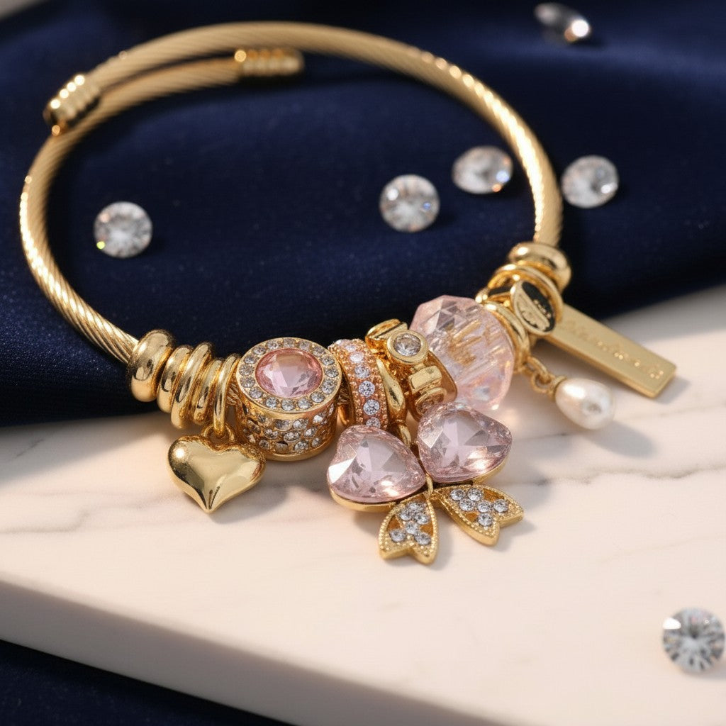 House of eLLe gold stainless steel bracelet featuring pink crystal bow charms, heart pendant, and pearl accents.