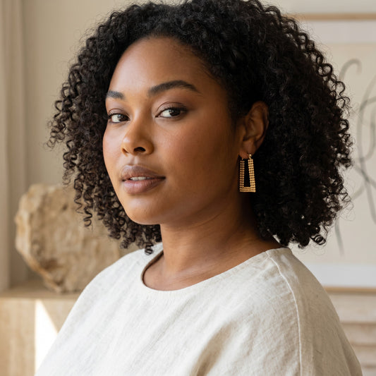 House of eLLe Always A Vibe gold rectangular textured hoop earrings worn by a woman with curly hair.