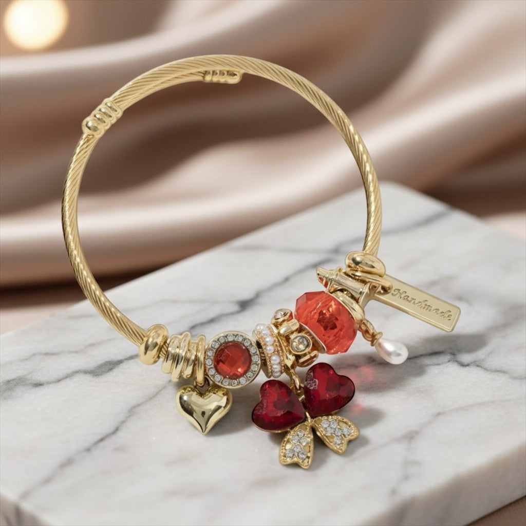House of eLLe gold stainless steel bracelet with red heart charms, crystals, and a handmade tag on marble surface