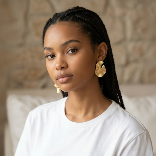 House of eLLe gold statement earrings with layered, fan-like design. Model wears a white t-shirt.