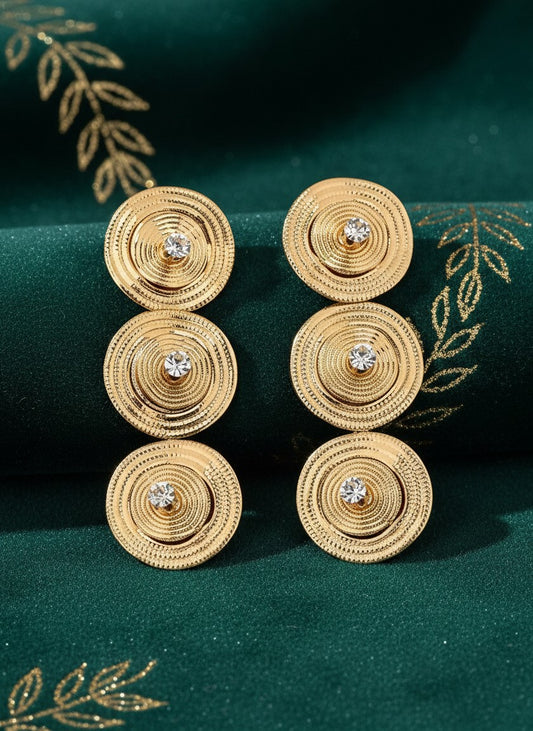 House of eLLe gold-tone triple circular drop earrings with central crystal accents on a dark green fabric background.