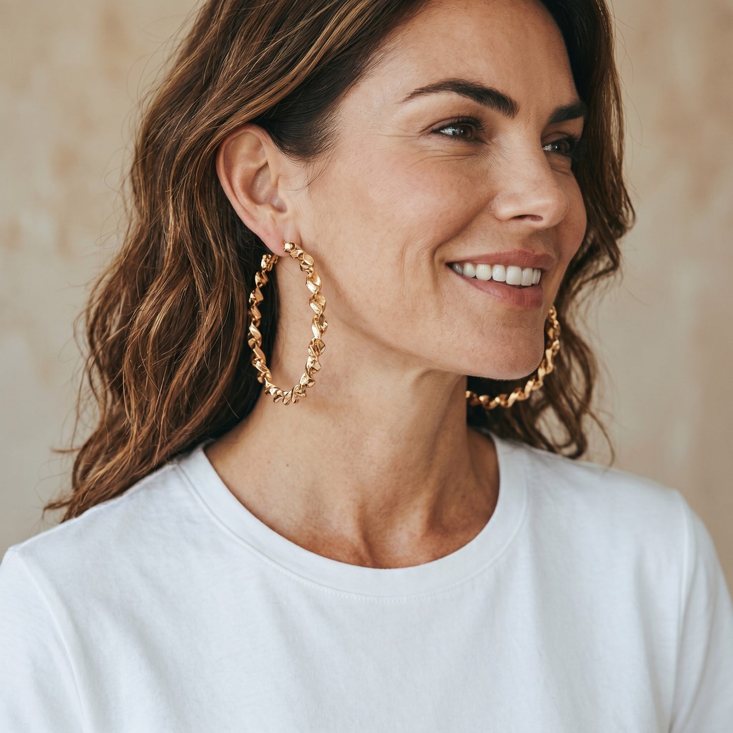 A woman wearing large gold House of eLLe My Twisted Hoops with a textured, spiraled design against a neutral background.