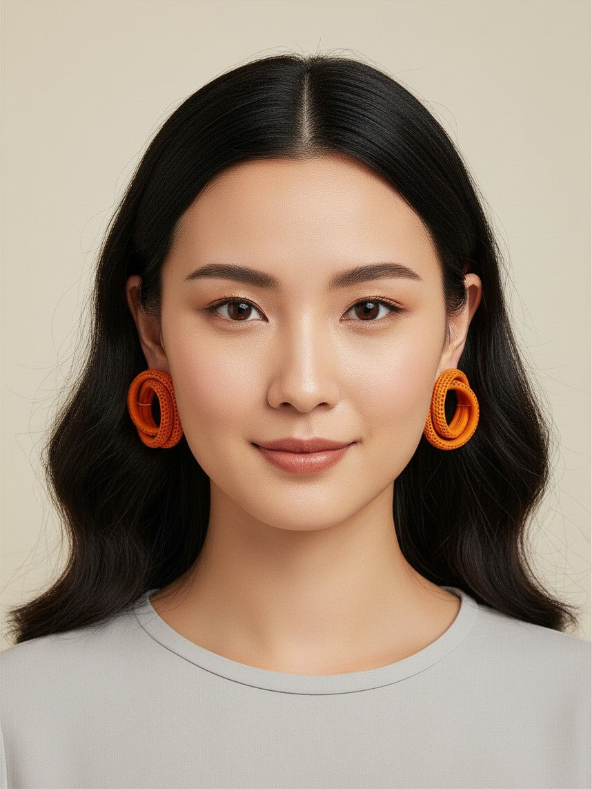 A woman wearing House of eLLe Sass In The City orange spiral textured statement earrings against a neutral background.
