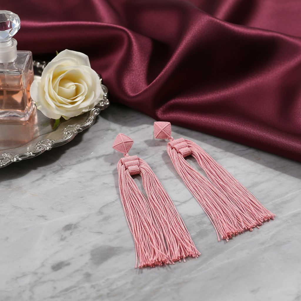 House of eLLe Queen Era pink tassel earrings with geometric studs on a marble surface with a white rose and perfume.