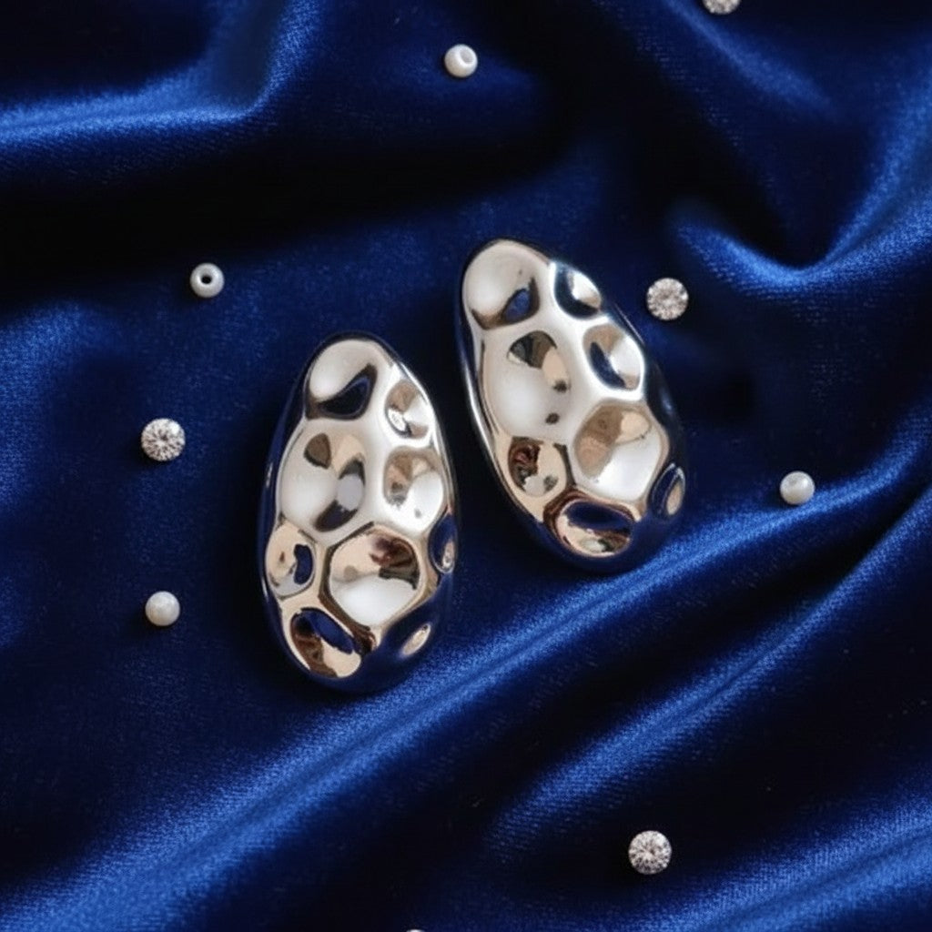 House of eLLe A Special Affair silver earrings with a textured, hammered metallic finish on a dark blue satin background