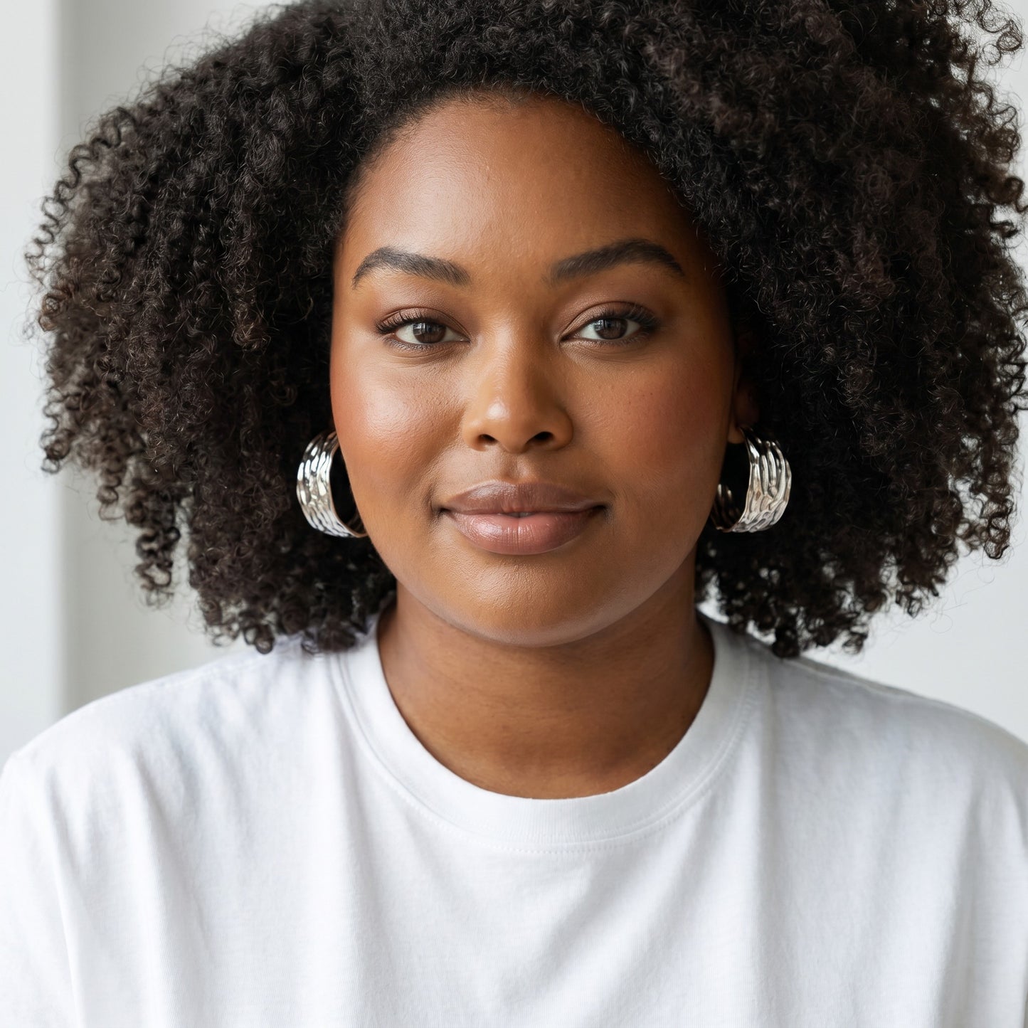 Model wearing House of eLLe Larger Than Life silver hoop earrings with a textured finish and white t-shirt.