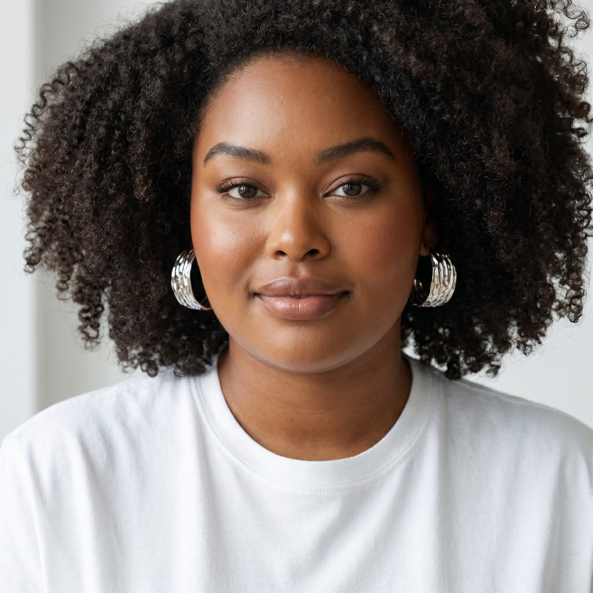 Model wearing House of eLLe Larger Than Life silver hoop earrings with a textured finish and white t-shirt.