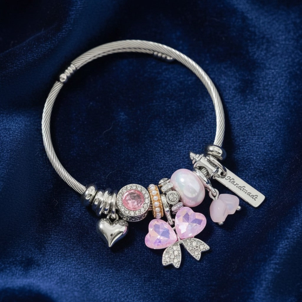 House of eLLe stainless steel charm bracelet featuring pink crystal bows, heart charms, and a handmade tag on blue velvet.