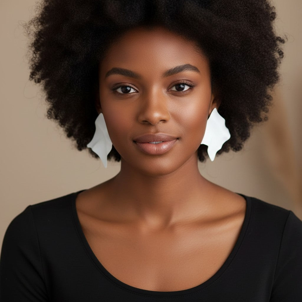 A woman with an afro wearing House of eLLe white Express Yourself earrings with an abstract, organic shape.
