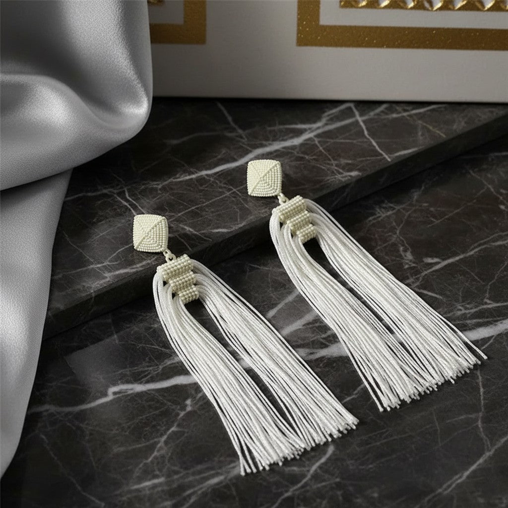House of eLLe Queen Era white beaded tassel earrings with square stud tops on a marble surface.