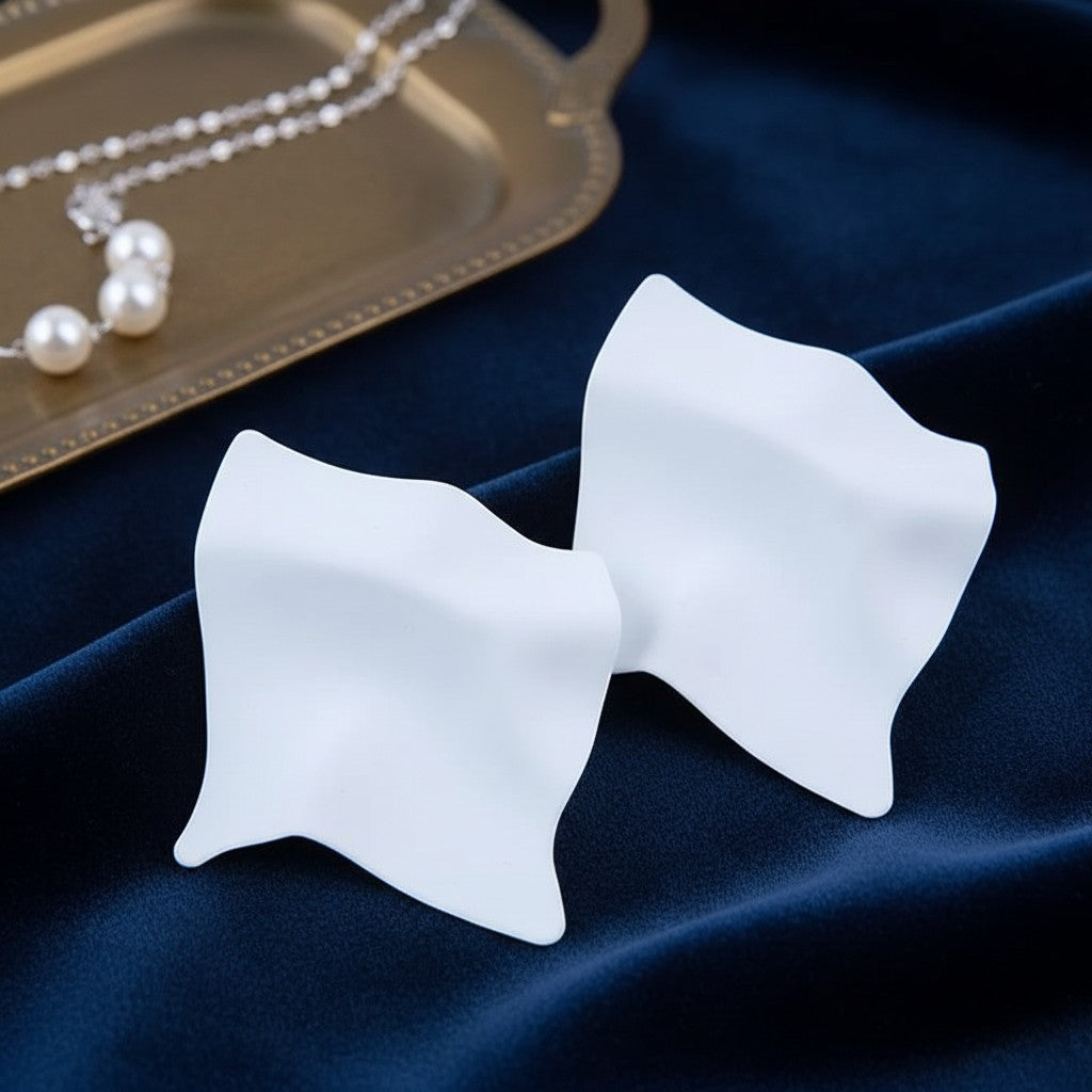 House of eLLe Express Yourself white matte sculptural earrings on a blue velvet background with a pearl necklace.
