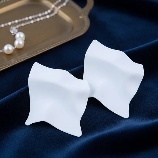 House of eLLe Express Yourself white matte sculptural earrings on a blue velvet background with a pearl necklace.