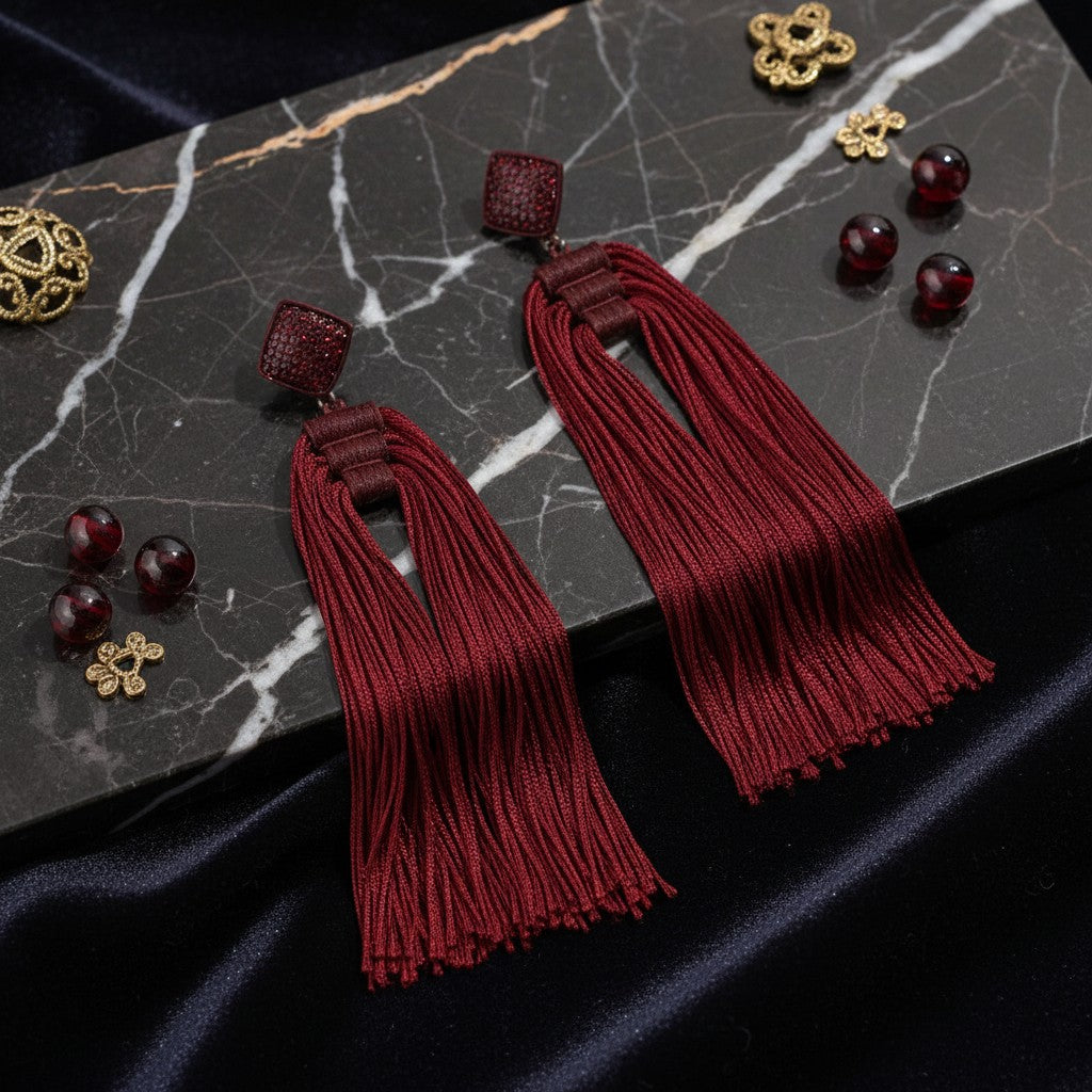 House of eLLe Queen Era wine red tassel earrings with square stud tops on a black marble surface.