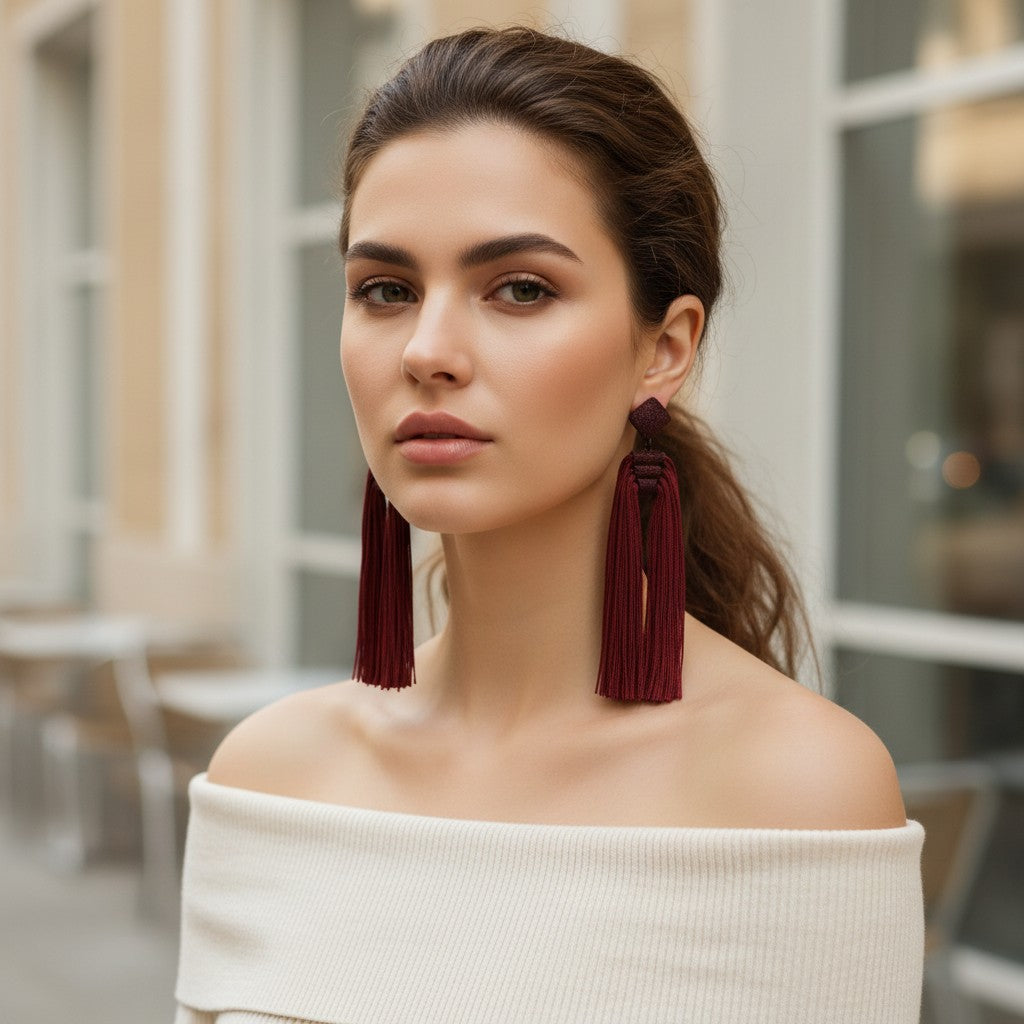 Model wearing House of eLLe Queen Era wine red tassel earrings with a white off-shoulder top