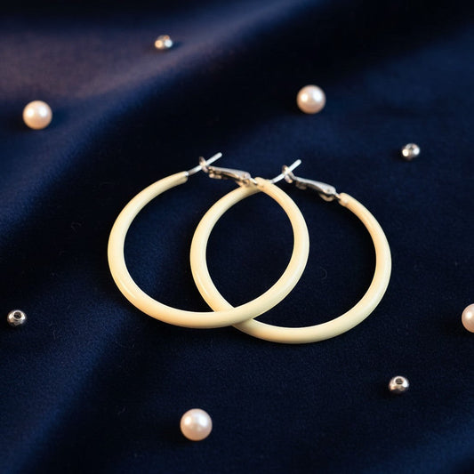 House of eLLe yellow hoop earrings resting on a dark blue fabric background with scattered pearl accents.